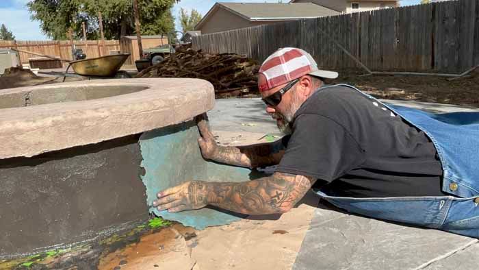 Man in overalls applying something to the side of a concrete structure. He is working outside.