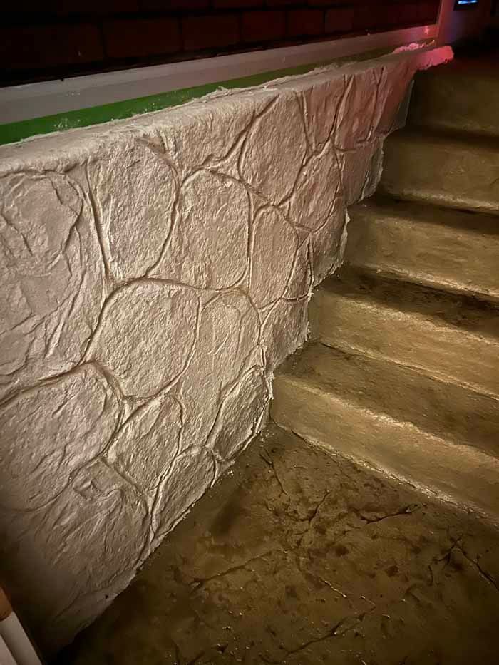 Textured concrete wall with steps, a pale-stone pattern, and a wet, dark floor.