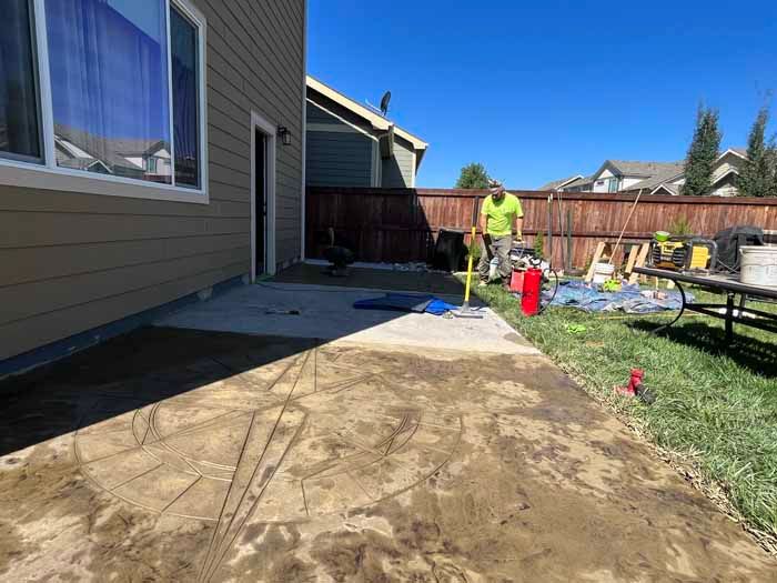Man leveling fresh concrete patio next to a house under a clear, blue sky.