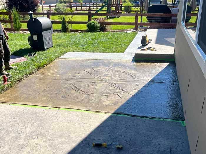 Concrete patio with a circular design, next to a grassy lawn and a house.
