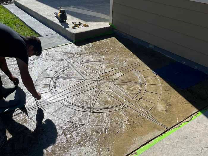 Person adding finishing touches to a compass rose design on wet concrete.