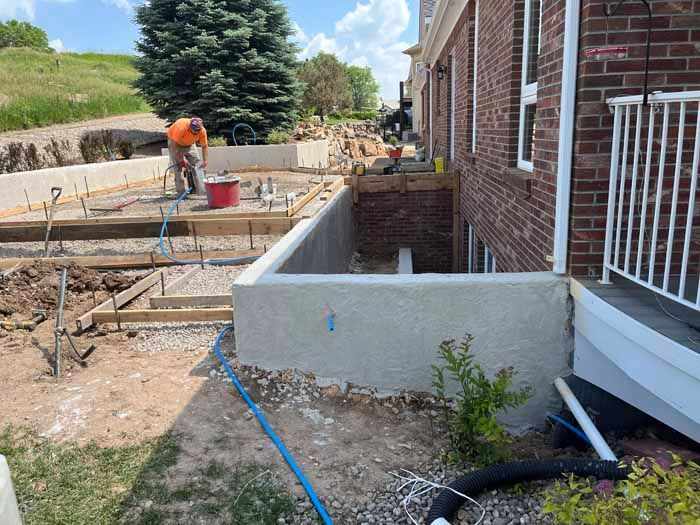 Construction site with worker by a brick building. Concrete forms and foundation work in progress.