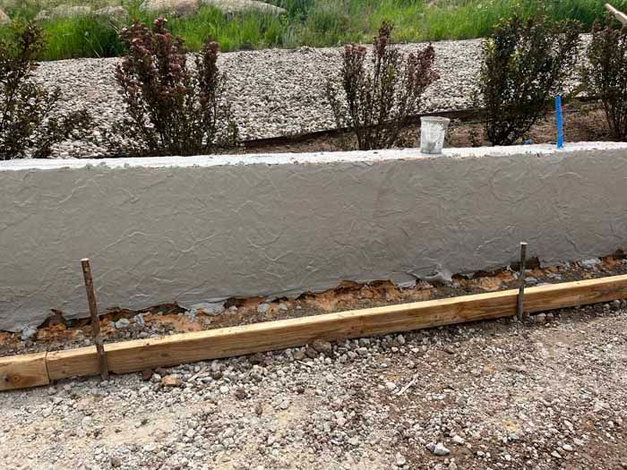 Freshly poured concrete retaining wall with wooden formwork and landscaping in background.
