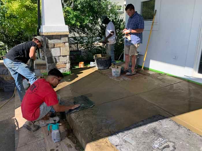 Four workers applying finish to a concrete patio outside a house.
