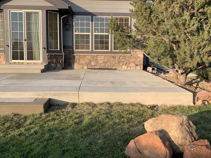 Concrete patio with a house, windows, and rocks in a grassy yard.