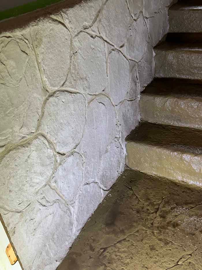 Stone-textured wall next to concrete stairs, likely interior. Light gray color.