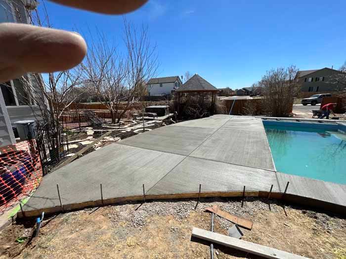 Newly poured concrete patio beside a pool on a sunny day.