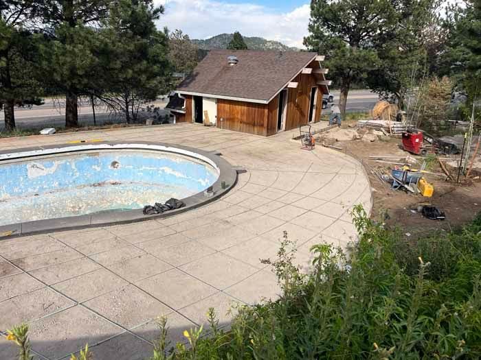 An empty pool with cracked blue tiles next to a brown wooden building under construction.