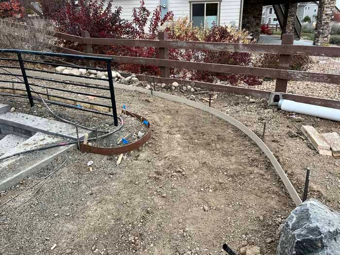 Construction site with a curved concrete curb being formed next to a fence and a set of stairs.