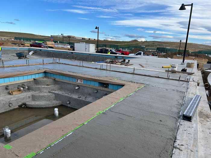 Construction site with unfinished pools and concrete walkways under a cloudy sky.