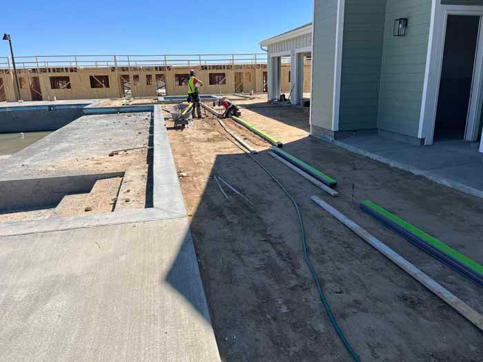 Construction site with pool, house, and workers; piping on the ground.