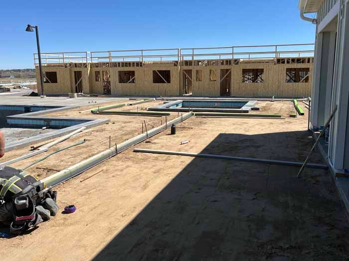Construction site with wooden framework, concrete forms, and partially built structures under a bright sky.