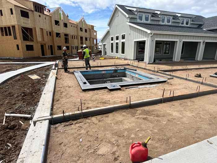 Construction site: Workers near a partially built pool. Buildings in the background; a gas can in the foreground.
