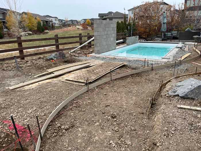 Construction site with a partially built pool, fence, and dirt path. Overcast day.