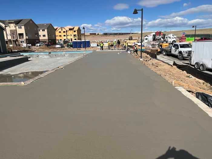 Construction site with freshly poured concrete path, pool, workers, trucks, and new buildings under construction.