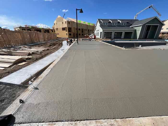 Construction site with wet concrete being smoothed; buildings in background.