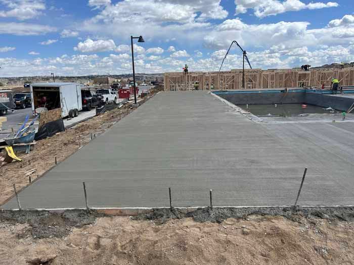 Newly poured concrete slab at a construction site; workers in the background, blue sky.