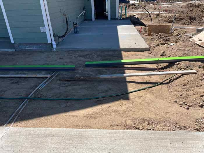 Construction site with concrete walkway and green pipes on dirt ground.