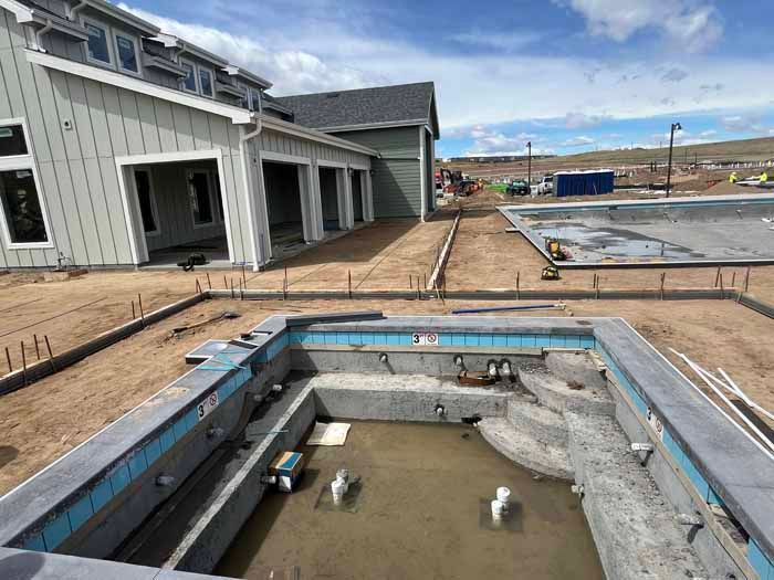 Construction site with two concrete swimming pools, adjacent to a house with a garage.