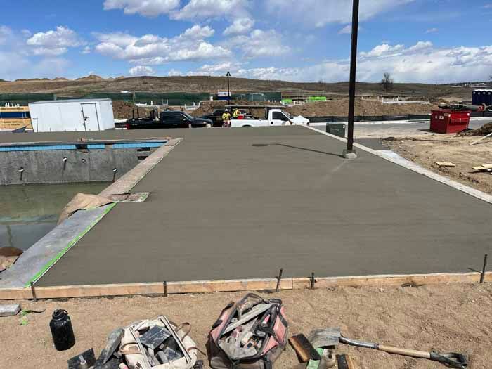 Newly poured concrete patio next to a pool under construction; sunny day.