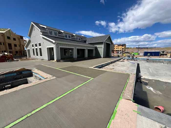 Construction site with a new concrete patio and pool, building in the background. Blue sky and sunny day.