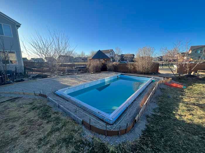 A rectangular pool in a backyard with a gazebo, clear blue sky, and surrounding landscaping.