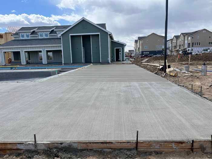 New concrete pathway leading to a teal-colored building under construction; surrounding construction site.