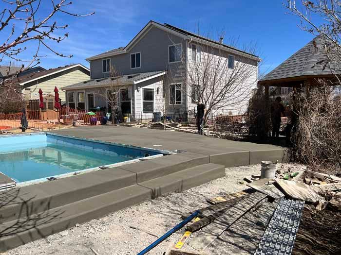 Backyard with a pool, concrete patio, two-story house, and gazebo on a sunny day.