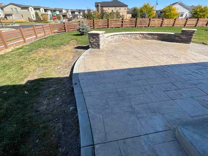Outdoor patio with stamped concrete, a retaining wall, and a wooden fence.