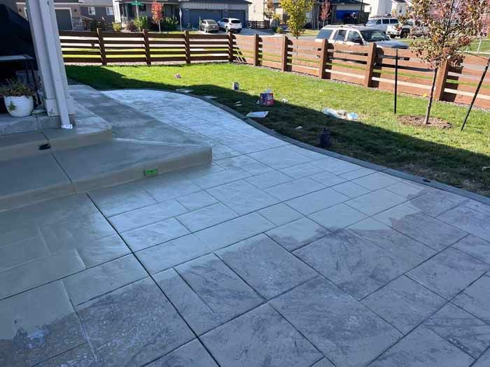 Newly poured concrete patio and walkway, pale gray color, in front of a house, with a fence and grass.