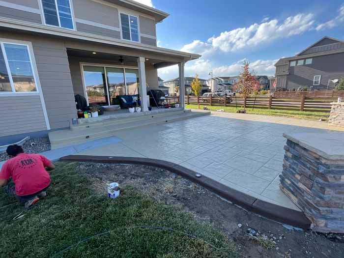 Man installing edging on concrete patio next to a house with a covered porch.