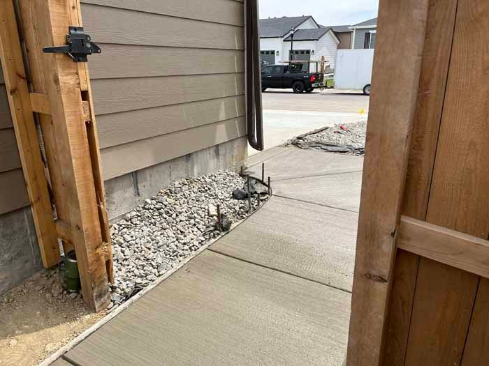 Concrete walkway, wooden gate, and gravel bed next to a house with tan siding.
