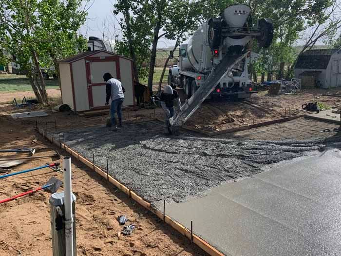 Concrete being poured by a truck into a form, two workers spread it out in a yard.