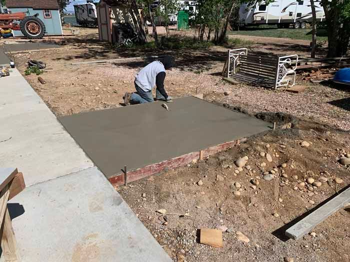 Person smoothing wet concrete on a square foundation, outdoors.