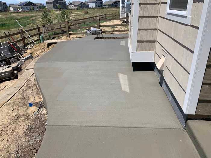 Newly poured concrete patio adjacent to a light-colored house.