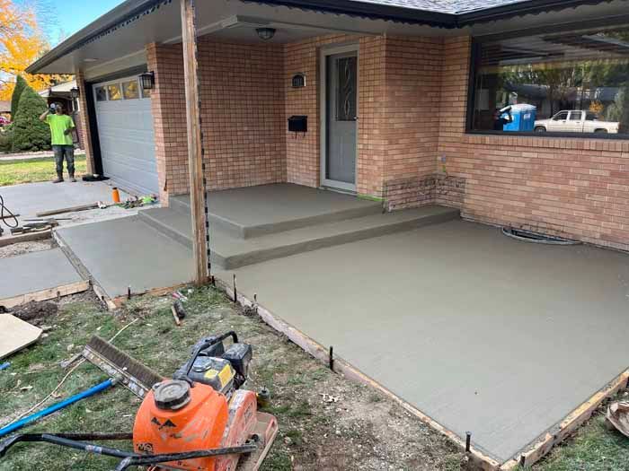 Freshly poured concrete patio and steps outside a brick house. Construction tools are visible.