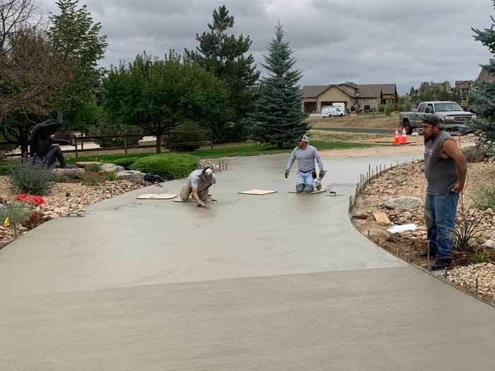 Workers smoothing concrete driveway. Cloudy day, residential area.