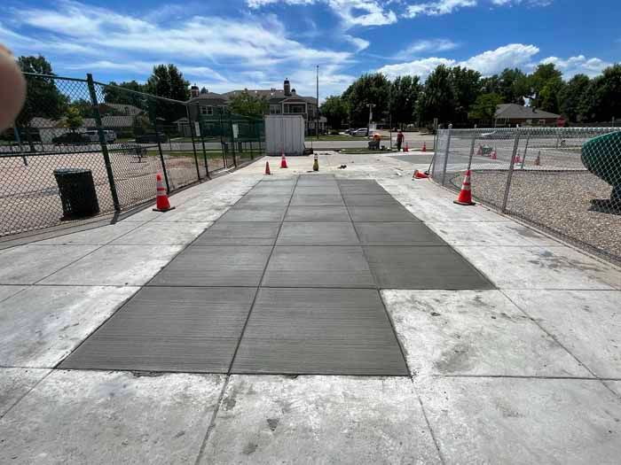 New concrete pavers being installed near a playground; orange cones mark the work area.