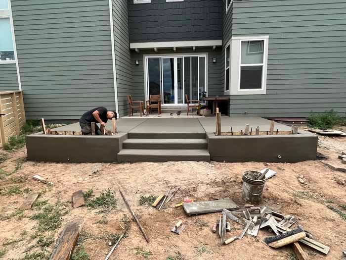 Man working on concrete steps and patio outside a house.