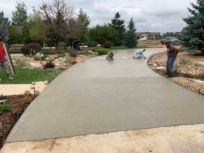 Workers smoothing fresh concrete driveway in a suburban setting.