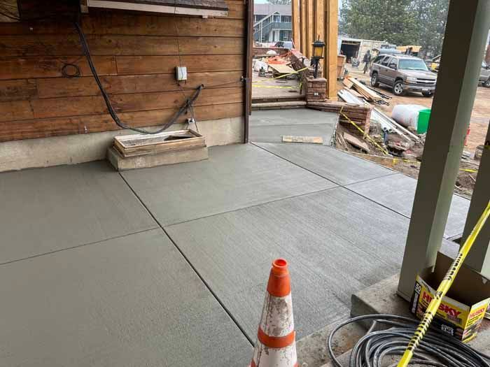 Newly poured concrete patio, construction site. Gray, rectangular slabs, orange traffic cone, and wood siding.