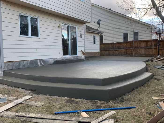Newly poured concrete patio with two steps leading from a house's sliding door to the yard.