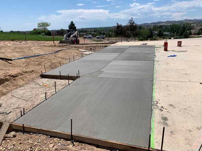 Freshly poured concrete sidewalk sections with wooden forms in a construction site.