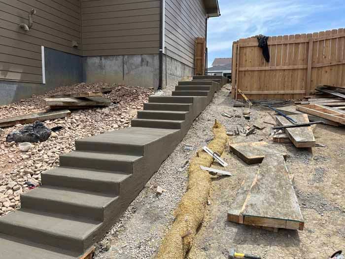 Concrete outdoor stairs under construction next to a house and wooden fence.