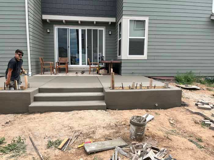 Man constructing a concrete patio with steps. Gray siding and sliding glass doors in the background.
