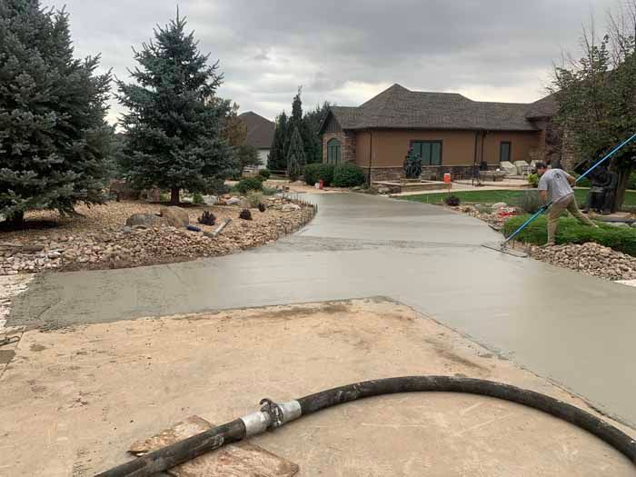 Man smoothing wet concrete driveway in front of a house on a cloudy day.