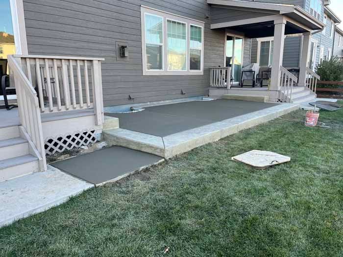 Concrete patio with steps, ramp, and edging on a grassy lawn next to a house.