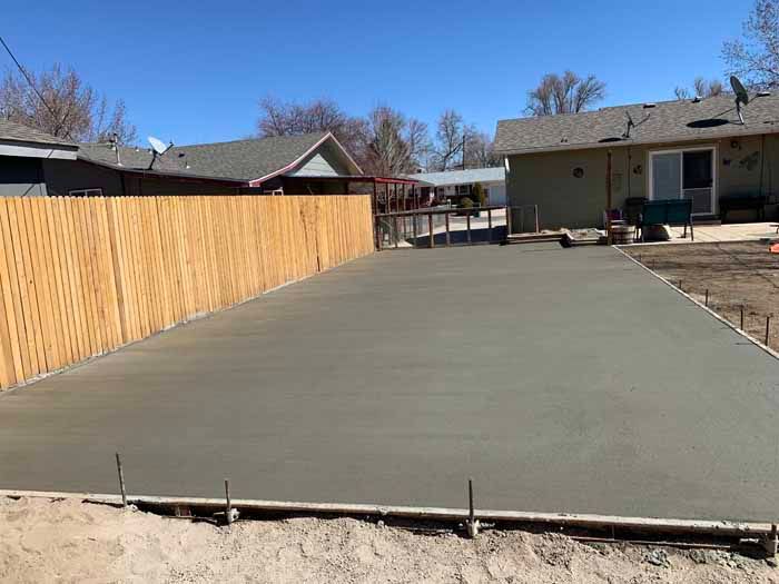 Newly poured concrete patio in a backyard with a wood fence and houses in the background.