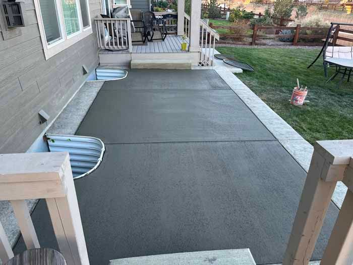 Freshly poured concrete patio with a step-up to a porch, and grass lawn.