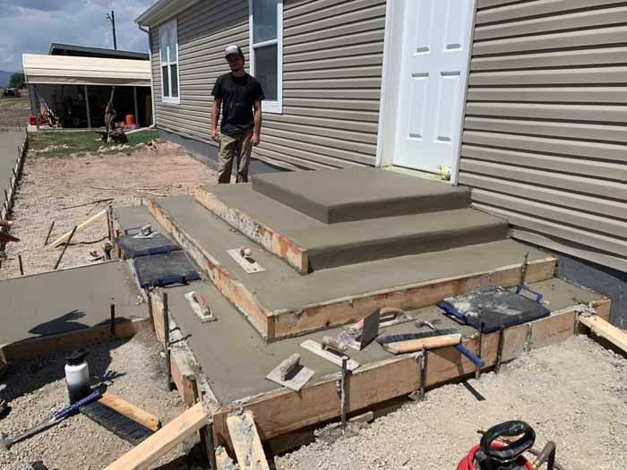 Man standing by newly poured concrete steps and walkway leading to a house.